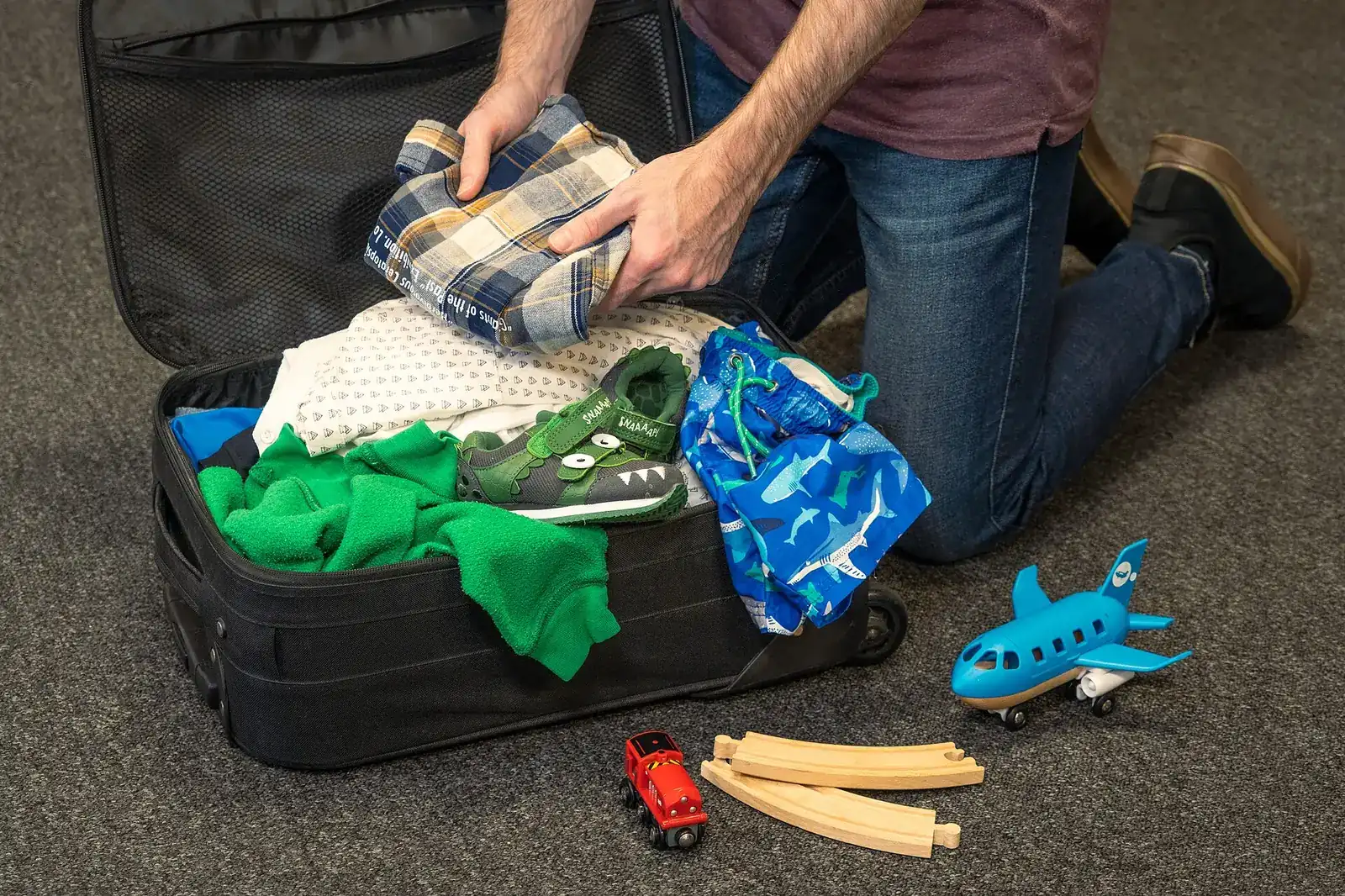 Padre o madre haciendo la maleta de su hijo con ropa, juguetes y un avión de juguete