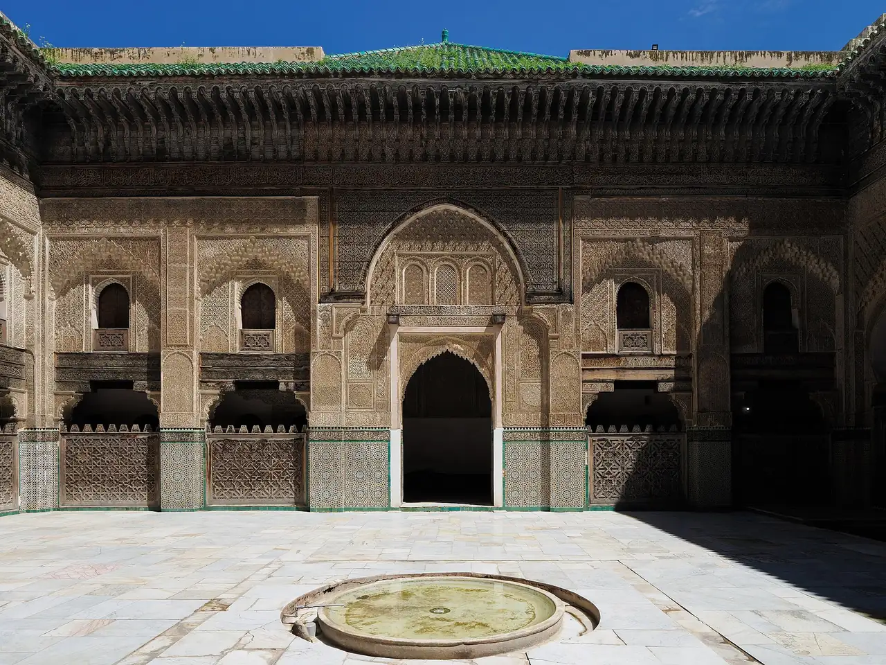 Yeserías talladas, madera de cedro y azulejos zellige en el patio de la Madraza Bou Inania