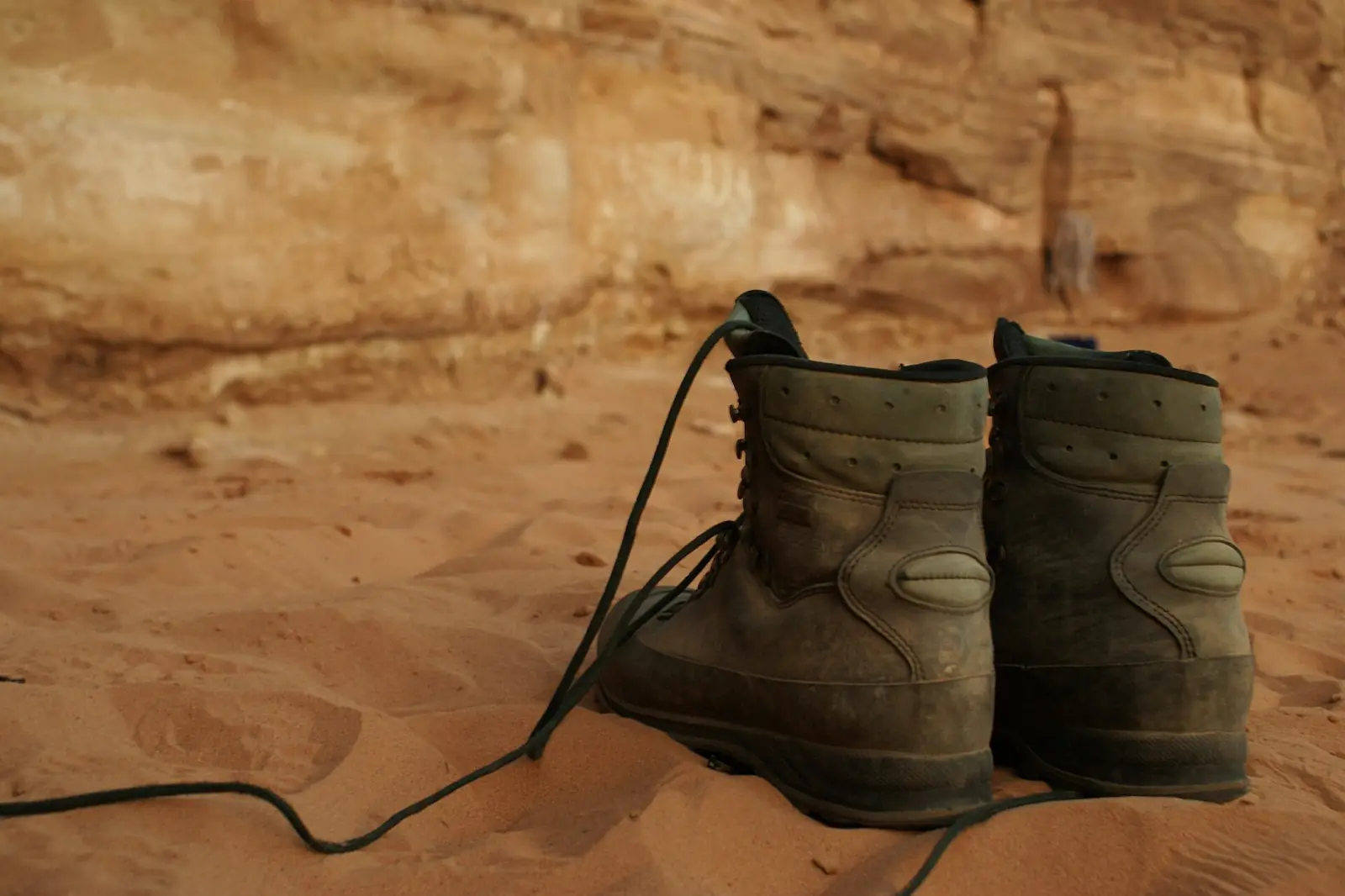 Par de botas de senderismo sobre la arena al pie de una pared rocosa en el desierto