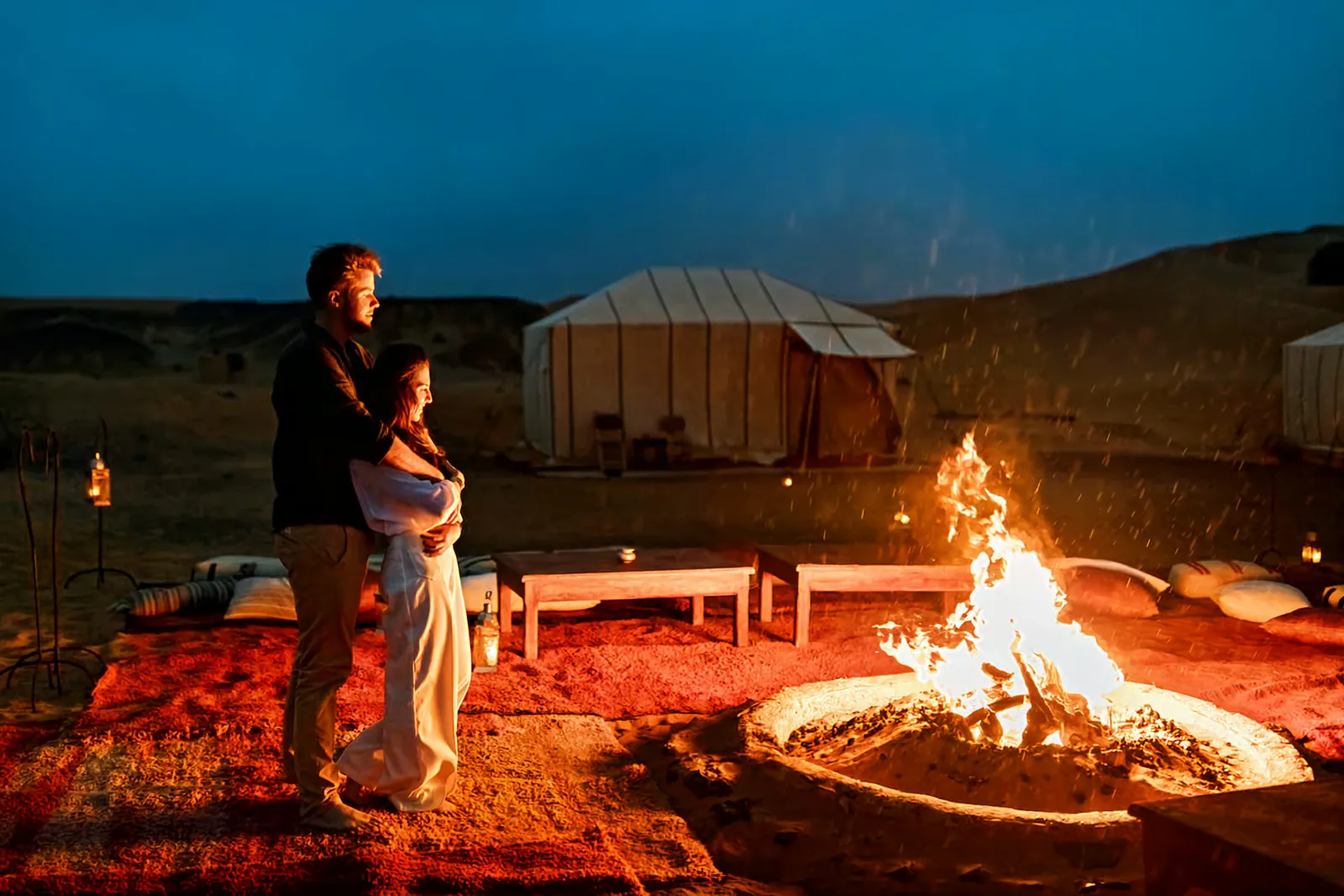 Traveller beside an evening fire with a desert tent in the background