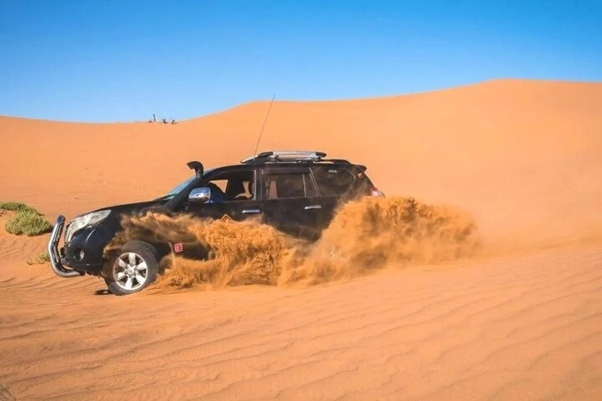 Four-wheel-drive vehicle travelling across orange desert sand