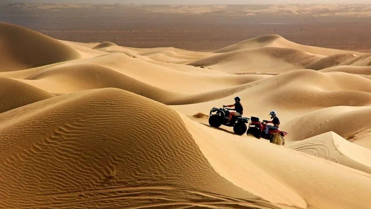 Two quad bikes riding over a dune