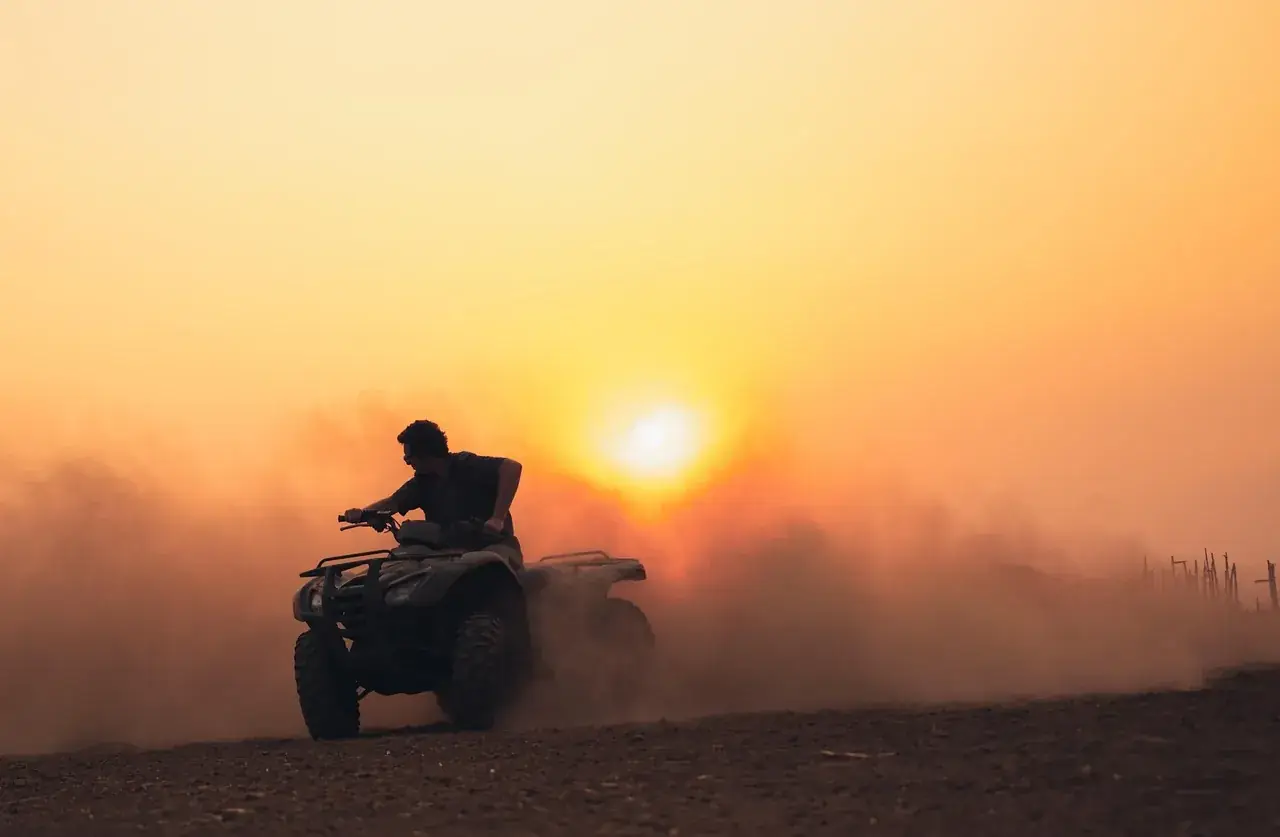 Quad bike riding through the dust at sunset
