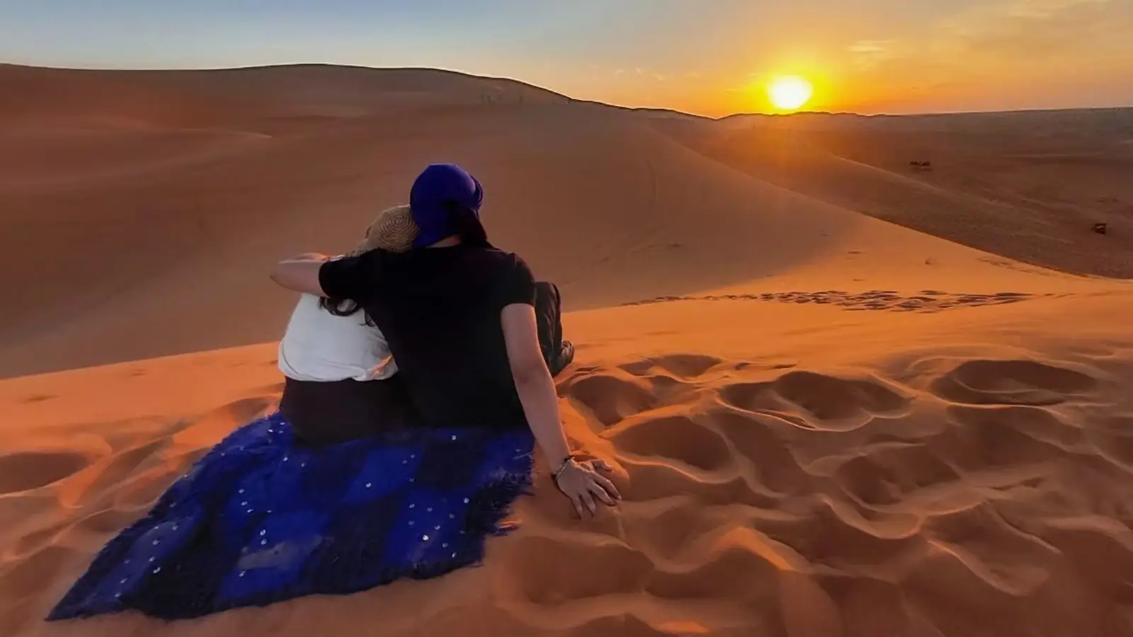 Pareja contemplando la puesta de sol desde la cresta de una duna en Erg Chebbi, Merzouga