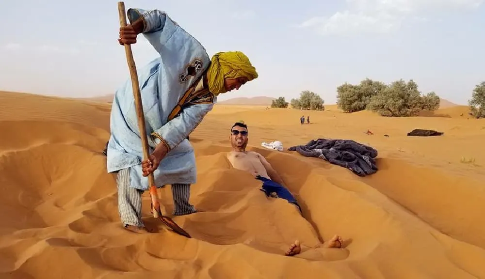 Berber therapist covering a guest in warm sand during a sand bath in Merzouga