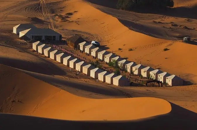 Hilera de jaimas de lujo blancas al pie de las dunas anaranjadas de Merzouga