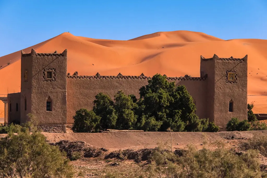 Kasbah tradicional de adobe frente a altas dunas naranjas bajo un cielo de invierno despejado en Merzouga