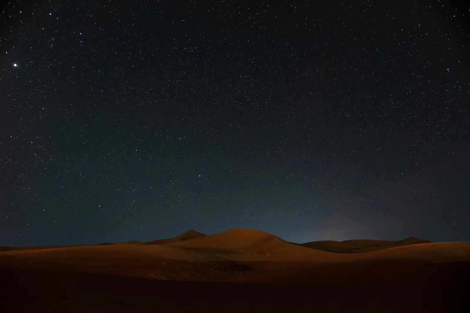 Cielo nocturno estrellado sobre el desierto en Marruecos con un tenue resplandor en el horizonte