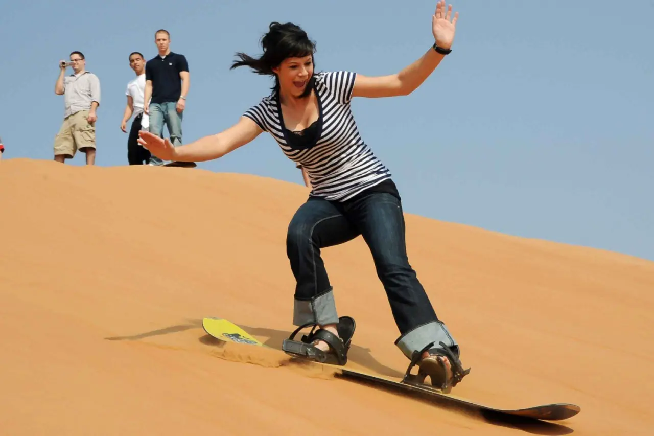 Woman sandboarding down a dune while friends watch