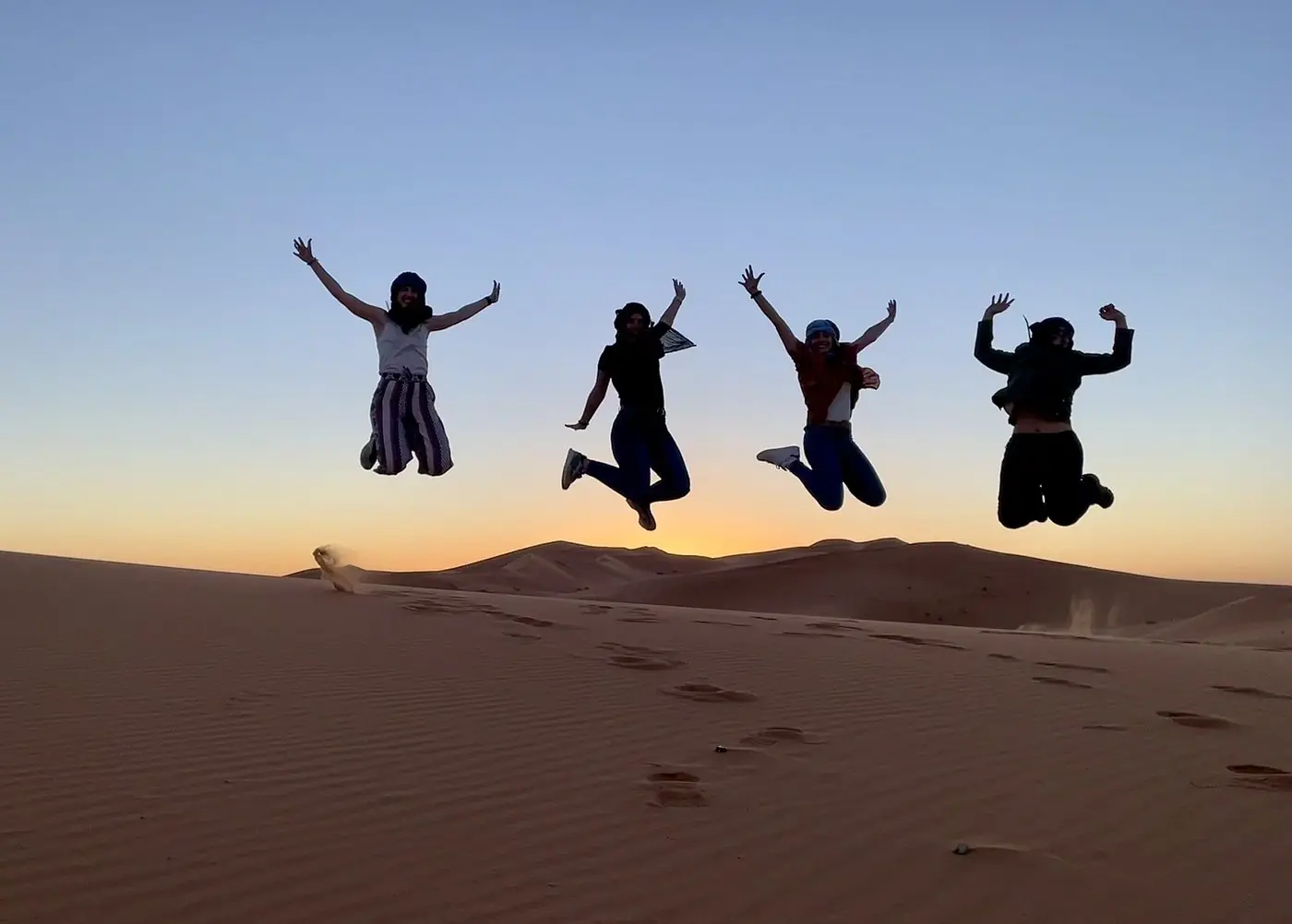Four travellers jumping on a dune crest at sunset