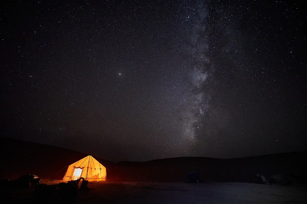 A lit tent beneath the Milky Way in the desert